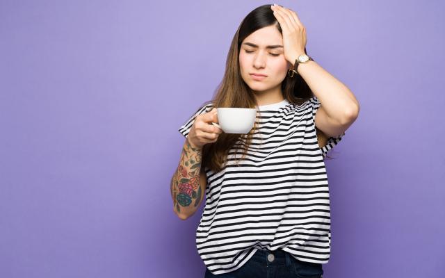 Een vrouw drinkt een kopje koffie en heeft hoofdpijn.