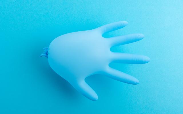 Een blauwe, opgeblazen rubberen handschoen tegen een blauwe achtergrond.