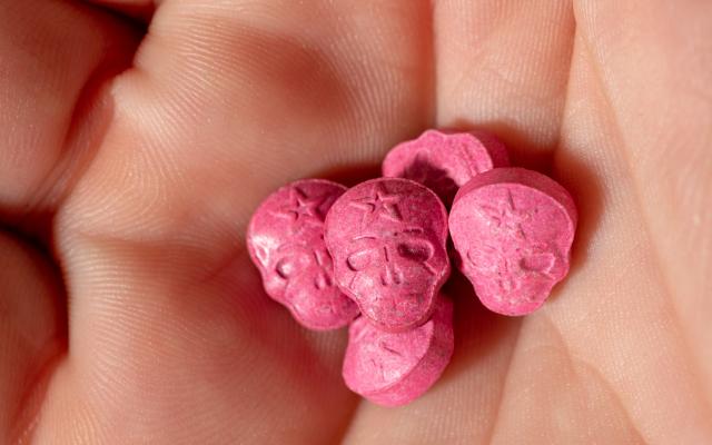 In een handpalm liggen roze pillen in de vorm van doodshoofden.