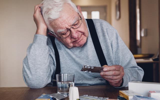 Een oudere man zit aan tafel en bekijkt een pillenstrip.