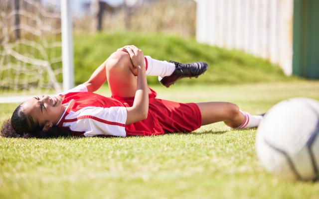 Voetbalster ligt op de grond en grijpt naar haar knie en vertrekt een gezicht van pijn.