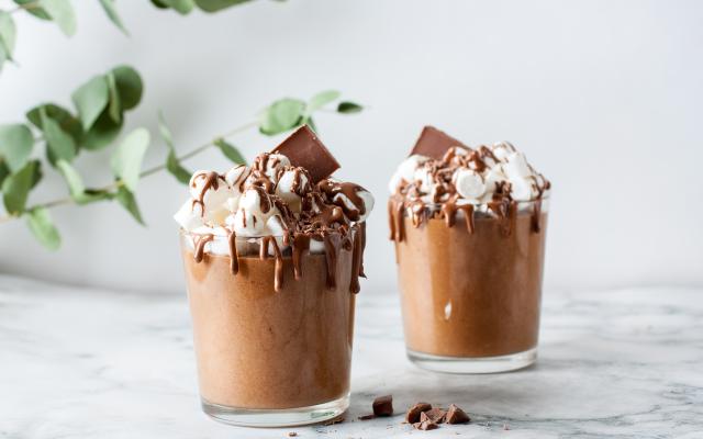 Twee glazen gevuld met chocolade en slagroom.