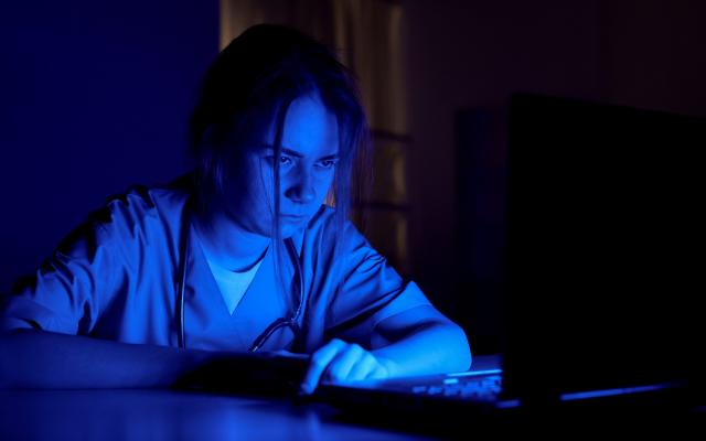 Een arts achter een laptop in het donker.