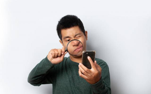 Een man kijkt met een vergrootglas naar een smartphone.