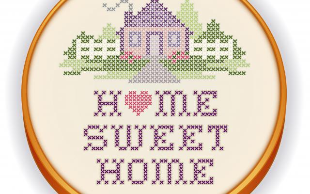 Een borduurring waar stof tussen gespannen is. Op de stof is een huis en de tekst 'home sweet home' geborduurd.