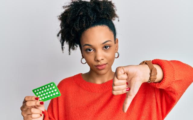 Een jonge vrouw heeft in haar rechterhand een strip pillen en doet met haar linkerhand een duim omlaag.