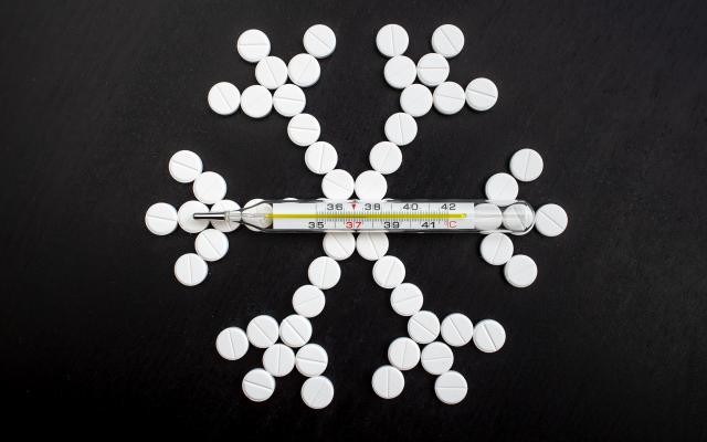 Pillen zijn neergelegd in de vorm van een sneeuwvlokje. Er ligt een thermometer bovenop.