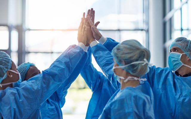 Een groepje artsen, gehuld in beschermende kleding, geeft elkaar een high five.