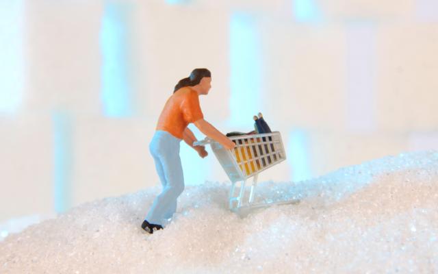 Een miniatuurfiguurtje loopt met een winkelwagentje over een berg suiker.