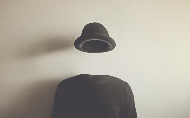 Een onzichtbaar persoon draagt een zwarte trui en een zwarte hoed.