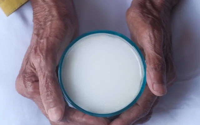 Een paar oude handen is gevouwen om een kop melk.