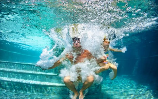 Twee personen zijn in een zwembad gesprongen en bevinden zich onderwater. De foto is onderwater genomen.