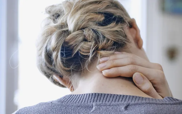 Een vrouw zit voorover gebogen met haar hand in haar nek.