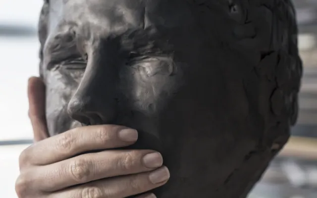 Beeld van een hoofd. Iemand heeft een hand over de mond van het beeld gelegd.