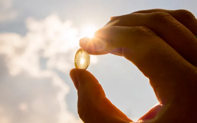 Een hand houdt een visoliecapsule tegen het zonlicht.