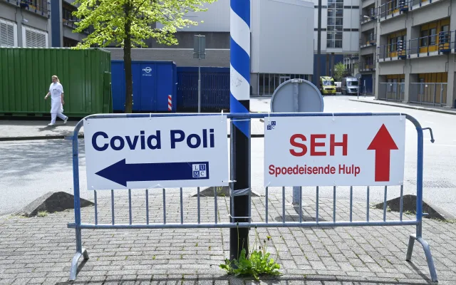 Foto: ANP Foto/Peter Hilz Een hek waar twee borden van het LUMC op bevestigd zijn. Op het linkerbord staat in het blauw 'Covid Poli' met een pijl naar links. OP het rechterbord staat in het rood 'SEH Spoedeisende Hulp' met een pijl naar boven.
