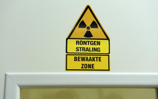 Gele waarschuwingsstickers met de teksten 'röntgenstraling" en "bewaakte zone" boven een deurpost.
