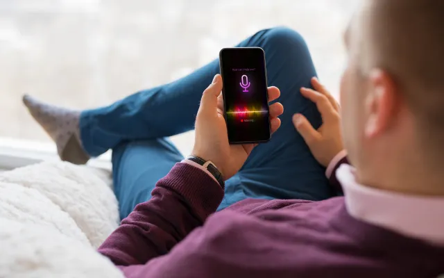 Een man kijkt op zijn telefoon. Op het scherm staat een microfoon en wordt er een geluidsopname afgespeeld.