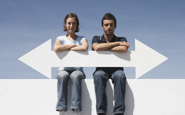 Twee mensen zitten op een muur en houden een pijl vast. De pijl wijst zowel naar links als naar rechts.