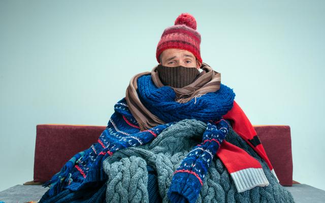 Iemand zit op een bank, gehuld in sjaals en truien.