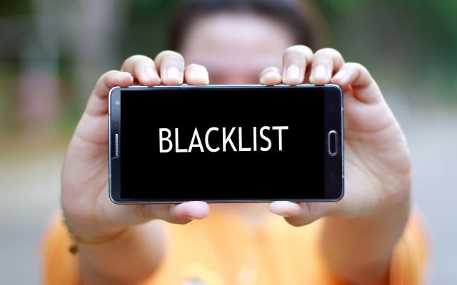Iemand houdt een smartphone vast. Op het scherm staat het woord 'blacklist'.