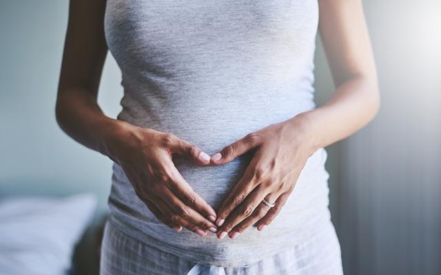 Handen vormen een hartje op een zwangere buik.