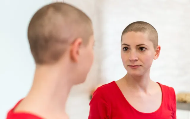 Foto: AndreaObzerova/iStock.com Stockfoto geposeerd door een model Dame met kortgeschoren haar die in de spiegel kijkt