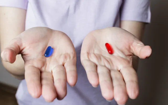 Foto: Viacheslav Dvoretskyi/iStock.com 2 handen met in de ene hand een rode pil, in de andere een blauwe