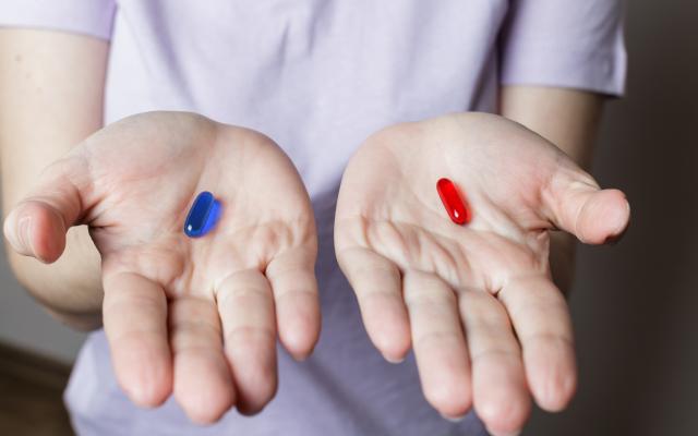 2 handen met in de ene hand een rode pil, in de andere een blauwe
