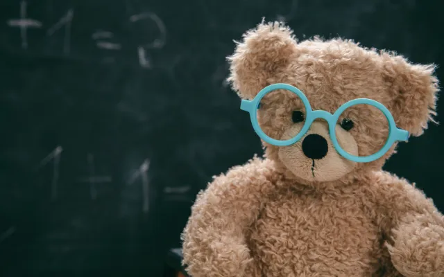 Teddybeer met een brilletje voor een schoolbord.
