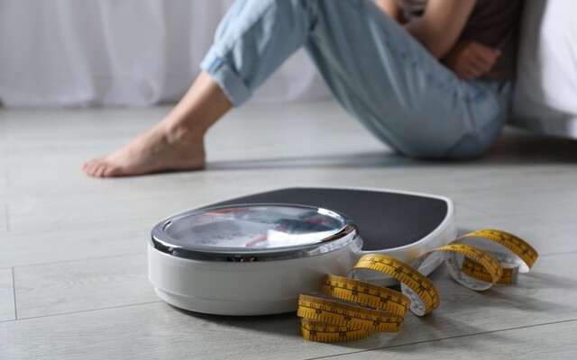 Foto van zittende vrouw met een weegschaal en meetlint