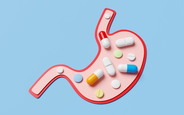 Een illustratie van een maag op een blauwe achtergrond, gevuld met verschillende soorten kleurrijke pillen