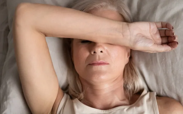 Een liggende vrouw die met haar arm haar ogen bedekt, wat een gevoel van vermoeidheid, hoofdpijn of rusteloosheid uitstraalt