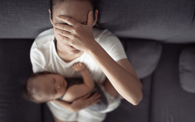 Een vermoeide vrouw die een slapende baby vasthoudt en met haar hand haar gezicht bedekt, wat een moment van uitputting of stress verbeeldt
