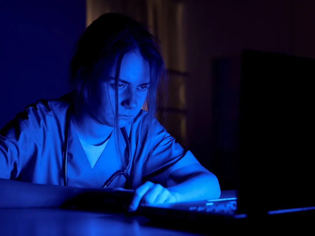Een arts achter een laptop in het donker.
