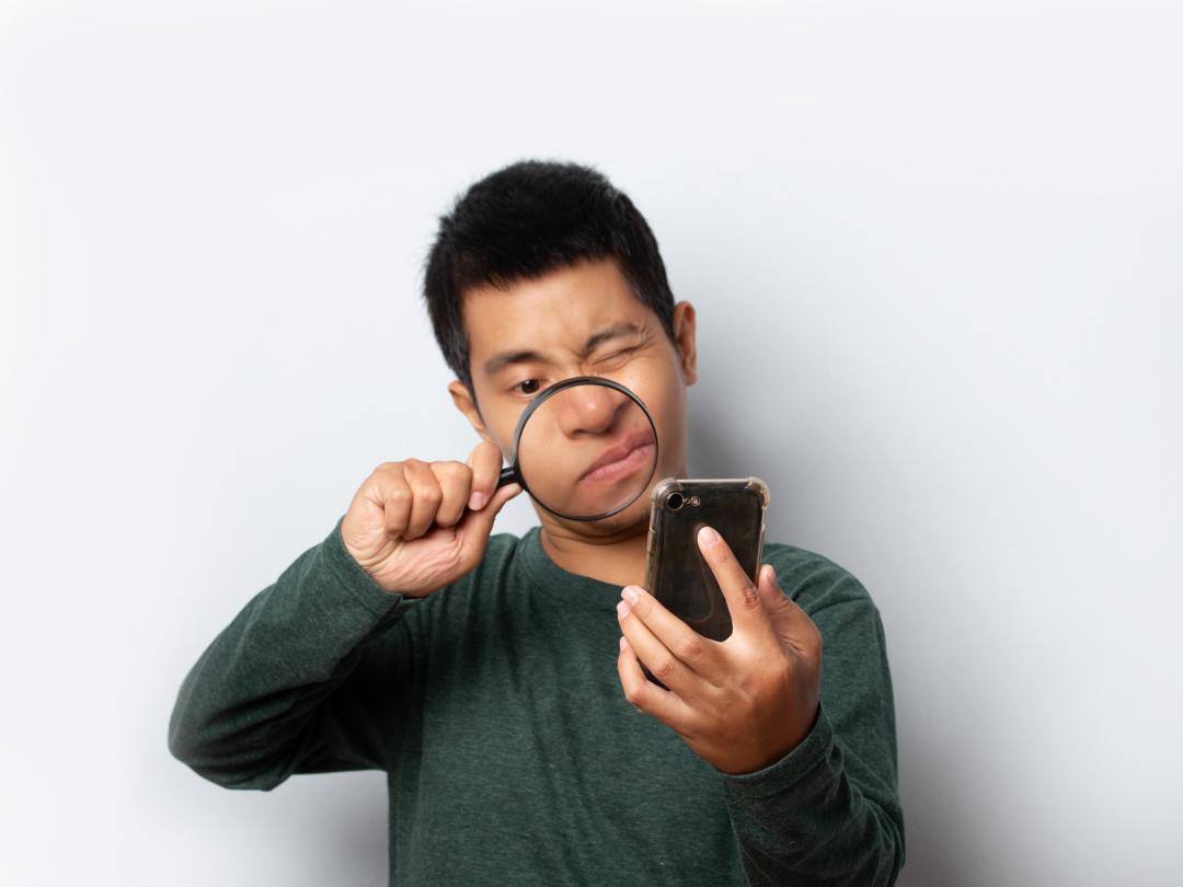 Een man kijkt met een vergrootglas naar een smartphone.