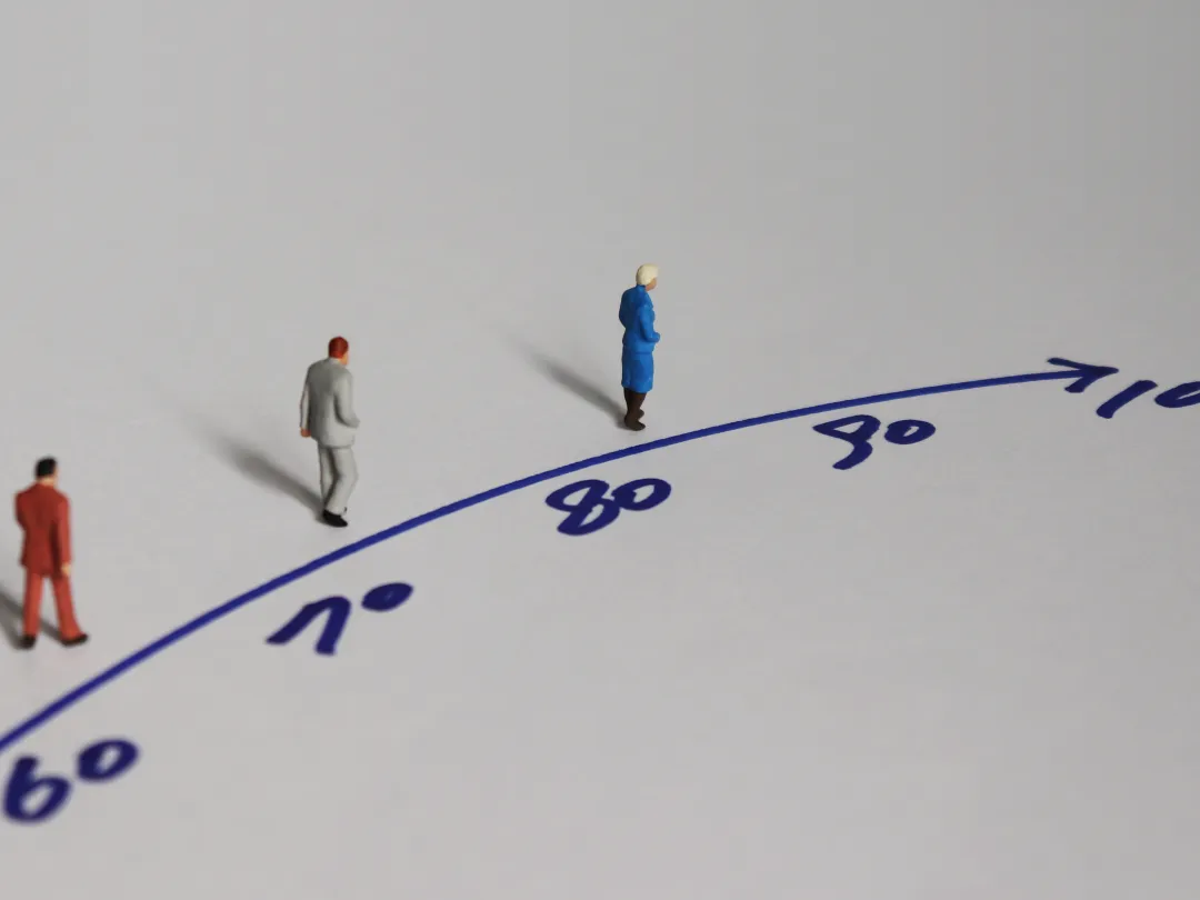 Drie kleine poppetjes staan op een tekening van een pijl. Langs de pijl staan getallen: 60, 70, 80, 90 en 100 aan het einde.