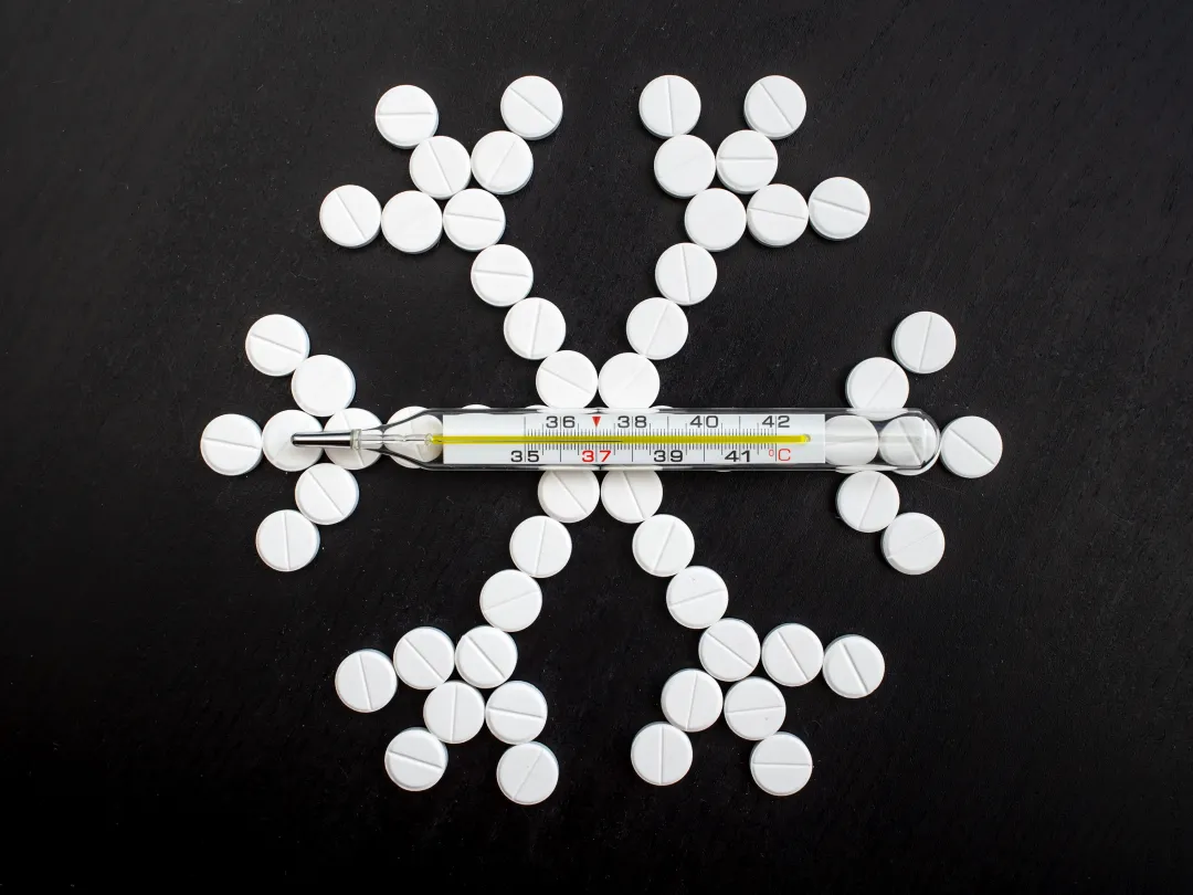 Pillen zijn neergelegd in de vorm van een sneeuwvlokje. Er ligt een thermometer bovenop.