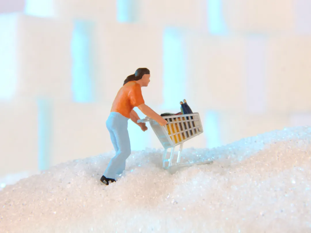Een miniatuurfiguurtje loopt met een winkelwagentje over een berg suiker.