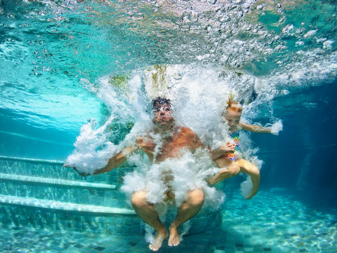 Twee personen zijn in een zwembad gesprongen en bevinden zich onderwater. De foto is onderwater genomen.