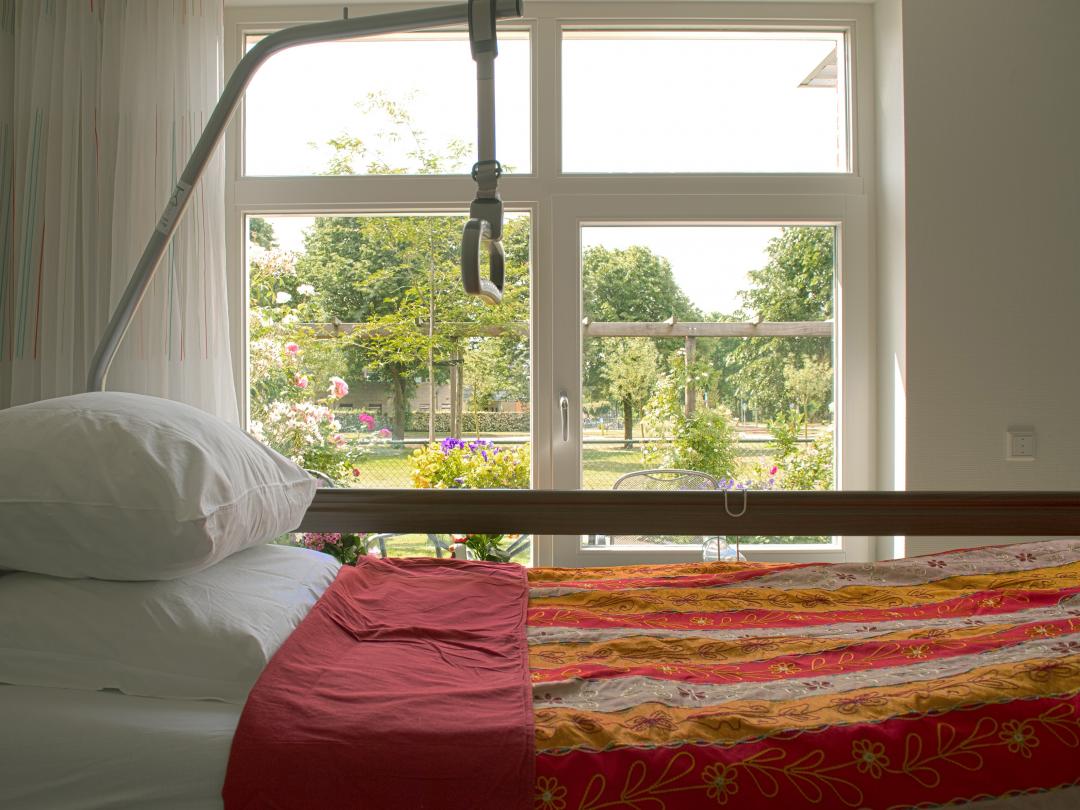 Een ziekenhuisbed naast een raam met uitzicht op een groene omgeving.