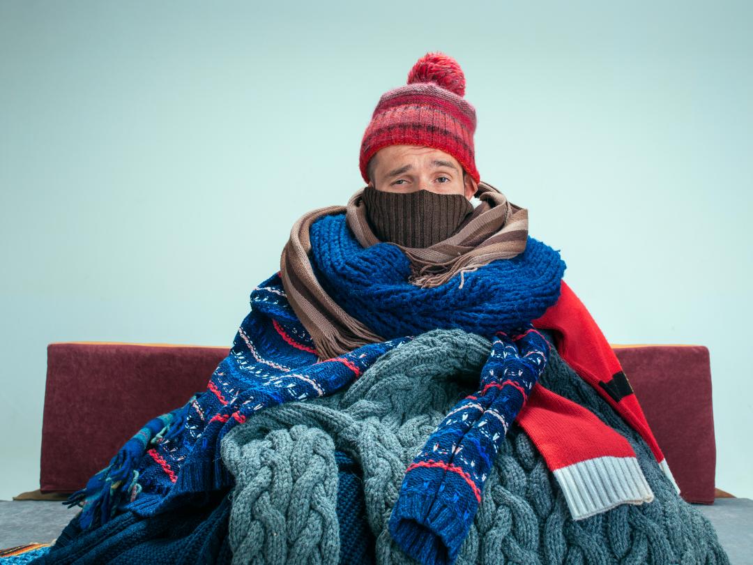 Iemand zit op een bank, gehuld in sjaals en truien.