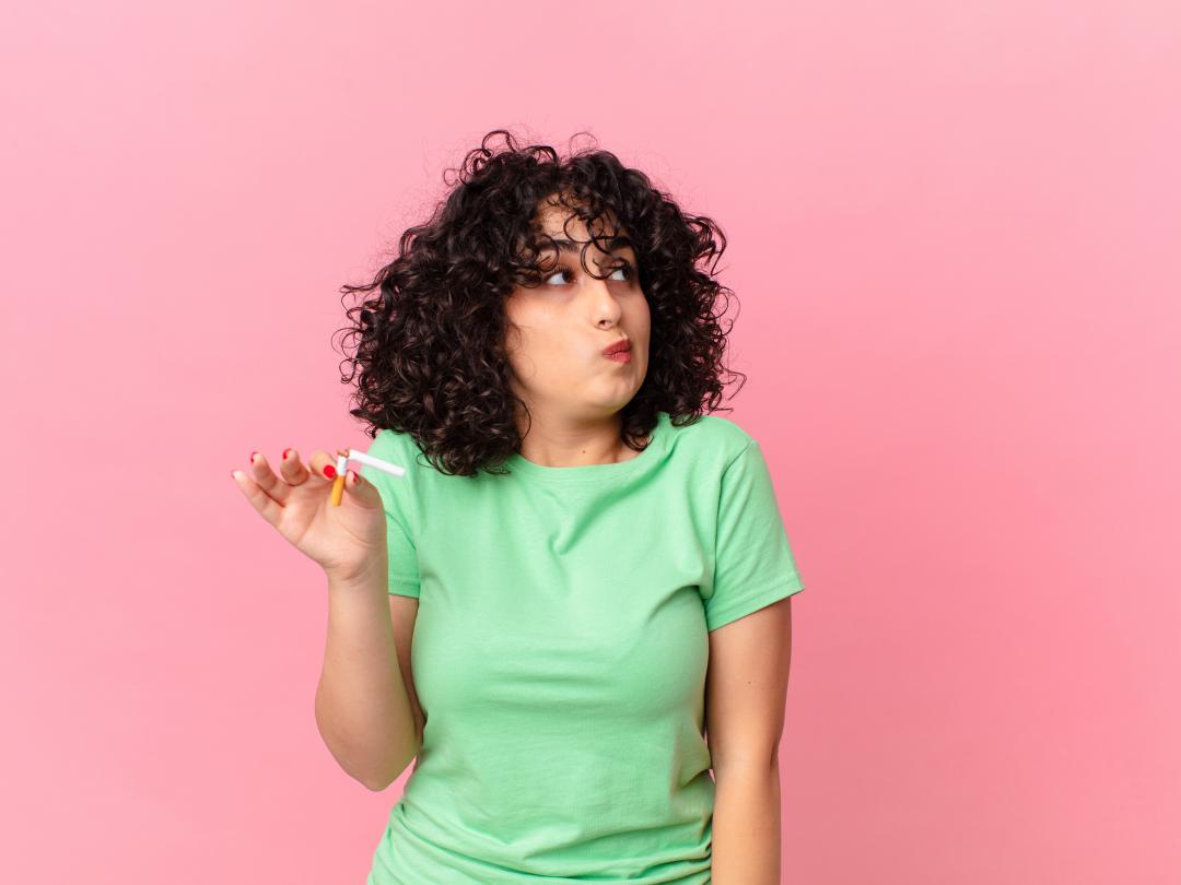 Een jonge vrouw houdt een gebroken sigaret vast.