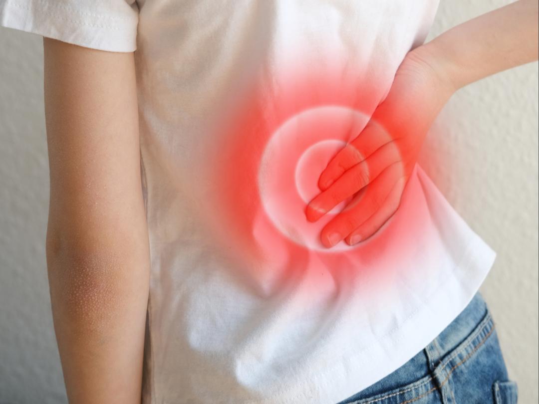 Een kind houdt zijn hand tegen zijn onderrug aan. Over deze plek is een rode cirkel geplaatst.