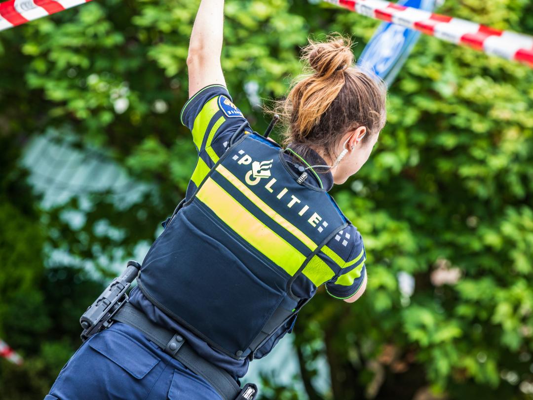 Politievrouw die rood-wit lint omhoog houdt.