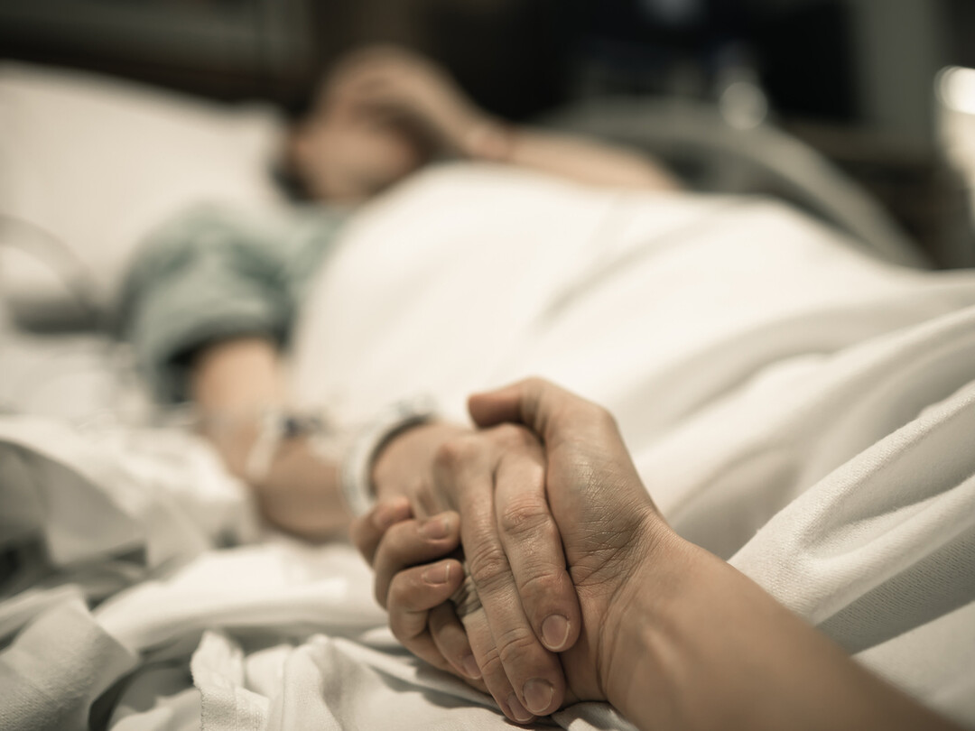 Iemand die een hand vasthoudt aan een ziekbed