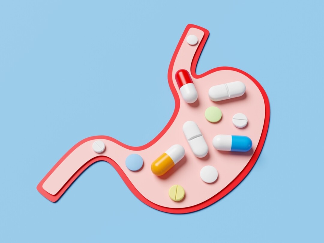 Een illustratie van een maag op een blauwe achtergrond, gevuld met verschillende soorten kleurrijke pillen