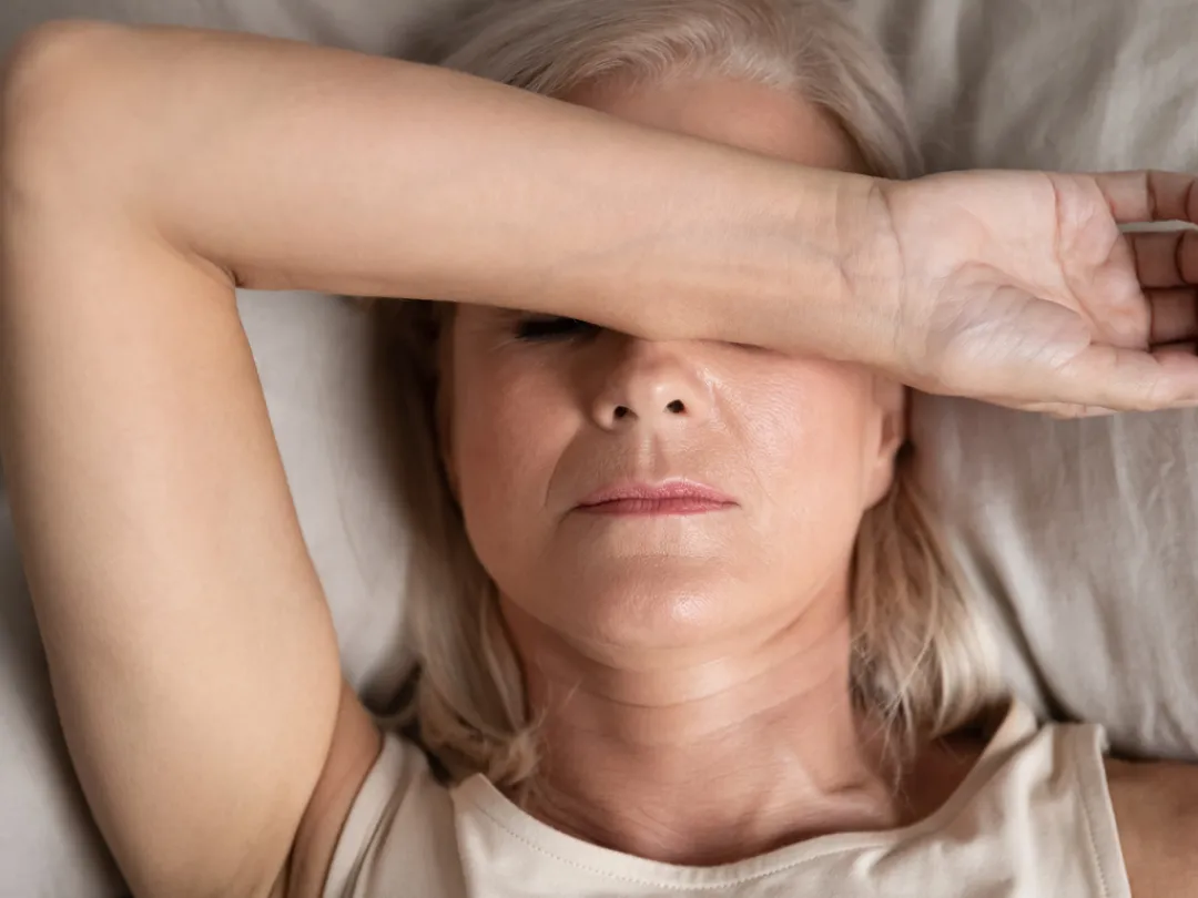 Een liggende vrouw die met haar arm haar ogen bedekt, wat een gevoel van vermoeidheid, hoofdpijn of rusteloosheid uitstraalt