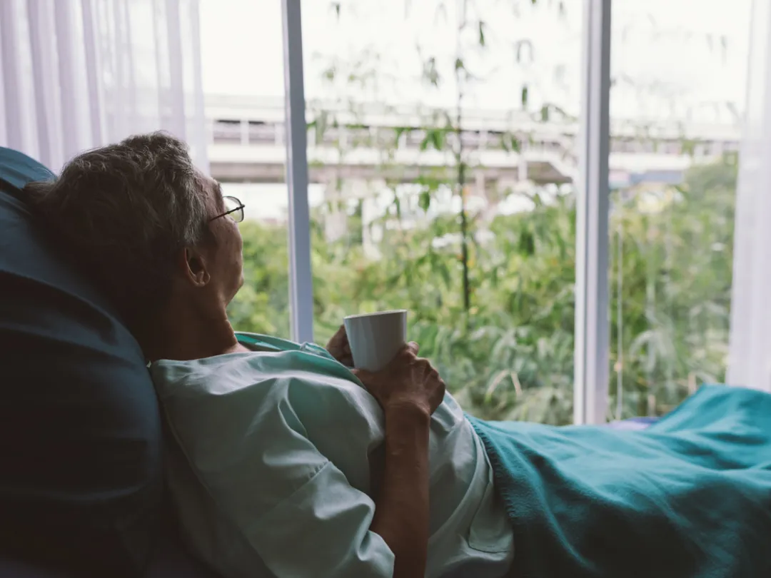 Iemand die vanuit een ziekenhuisbed naar buiten kijkt