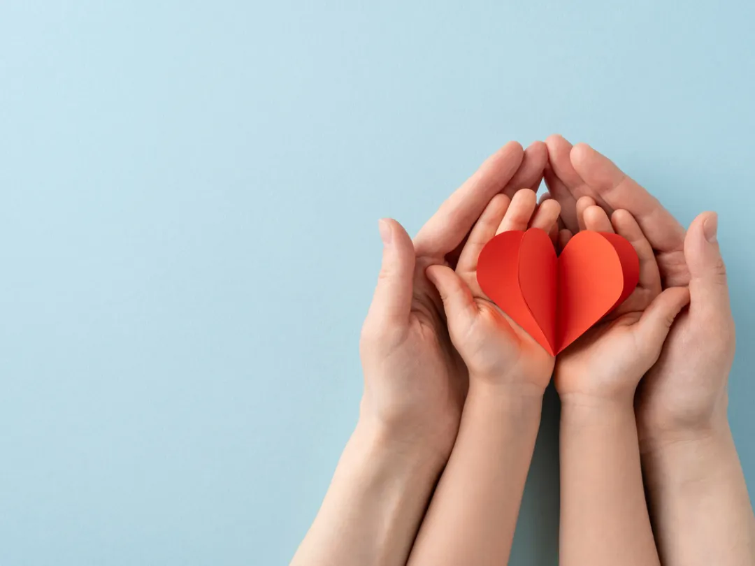 Volwassen handen met daarin kinderhanden met een hart